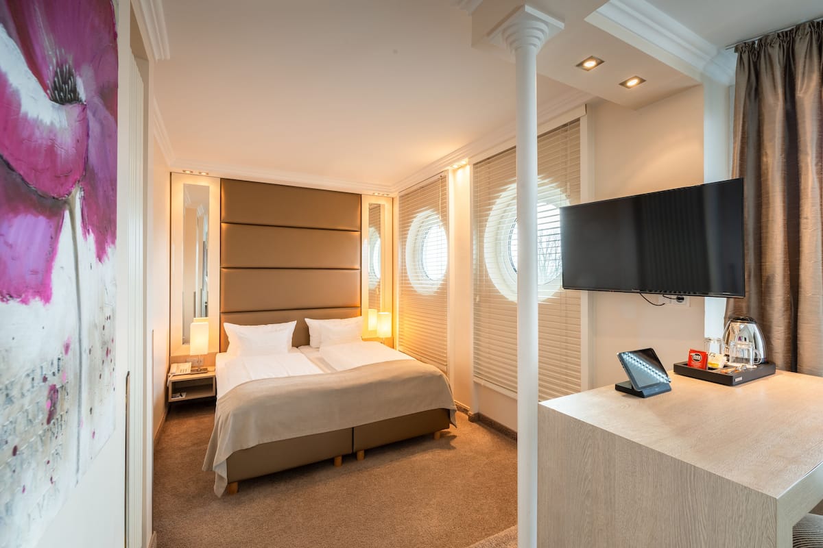 Ein Hotelzimmer mit Bett, Nachttisch, Lampe, Fernseher und einer Kaffeemaschine.