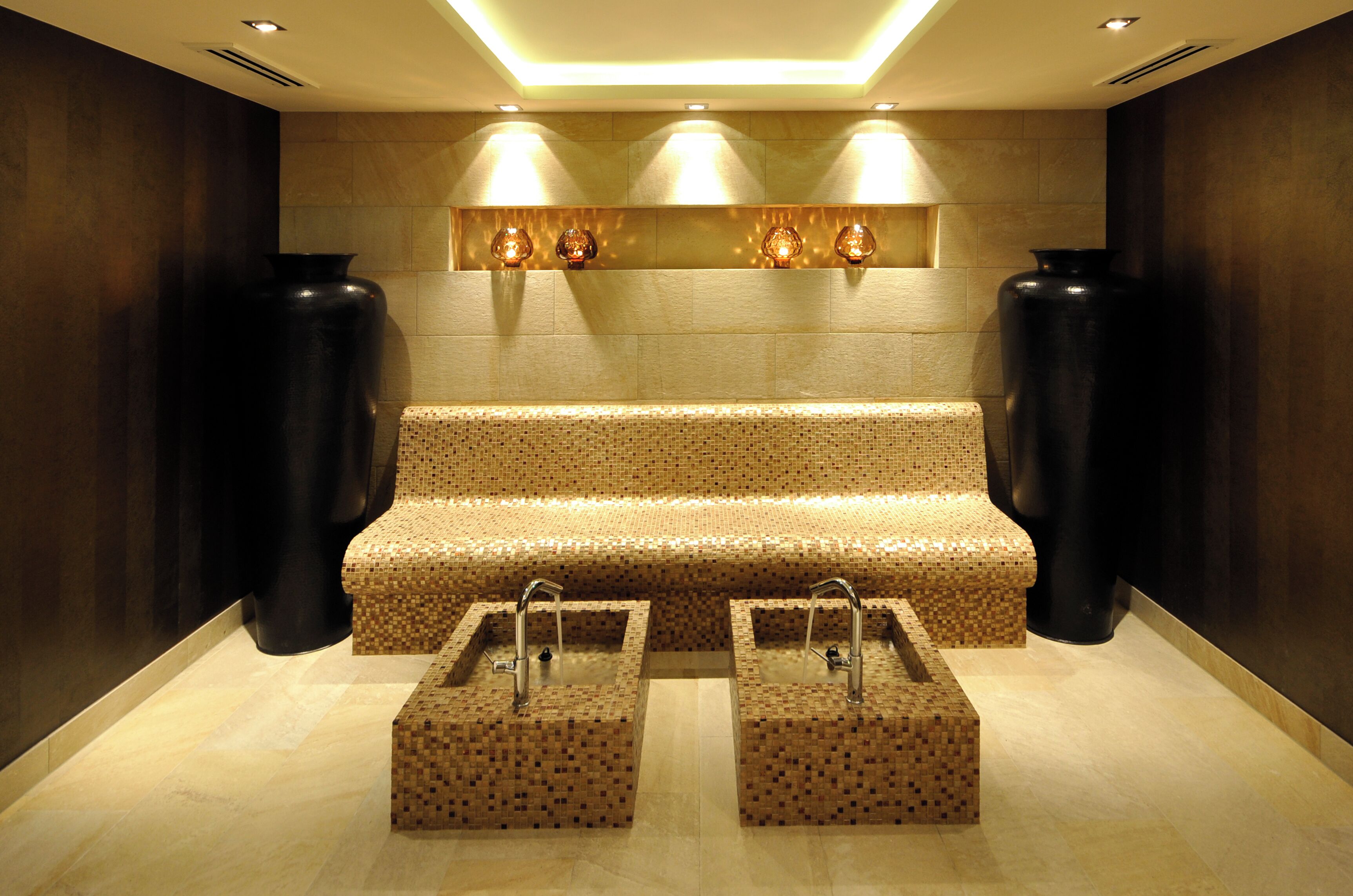 Une salle de bain moderne avec un banc, deux vasques et des vases décoratifs.