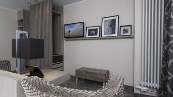 A modern hotel room with a sofa, a small table, a TV, and a wall with framed pictures.