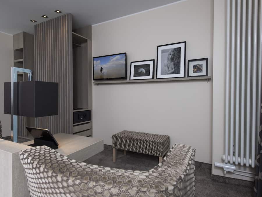 A modern hotel room with a sofa, a small table, a TV, and a wall with framed pictures.