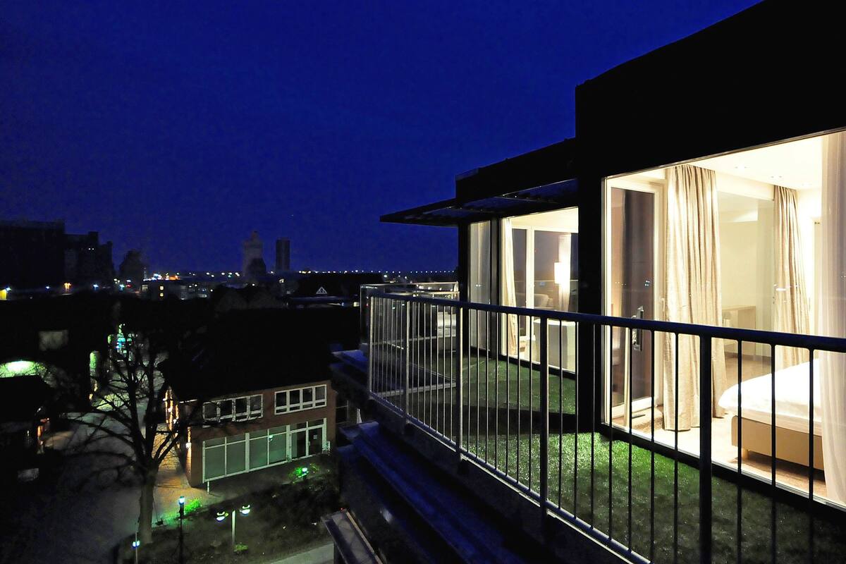 Ein modernes Hotelzimmer mit Balkon, großen Fenstern und Blick auf die nächtliche Skyline.