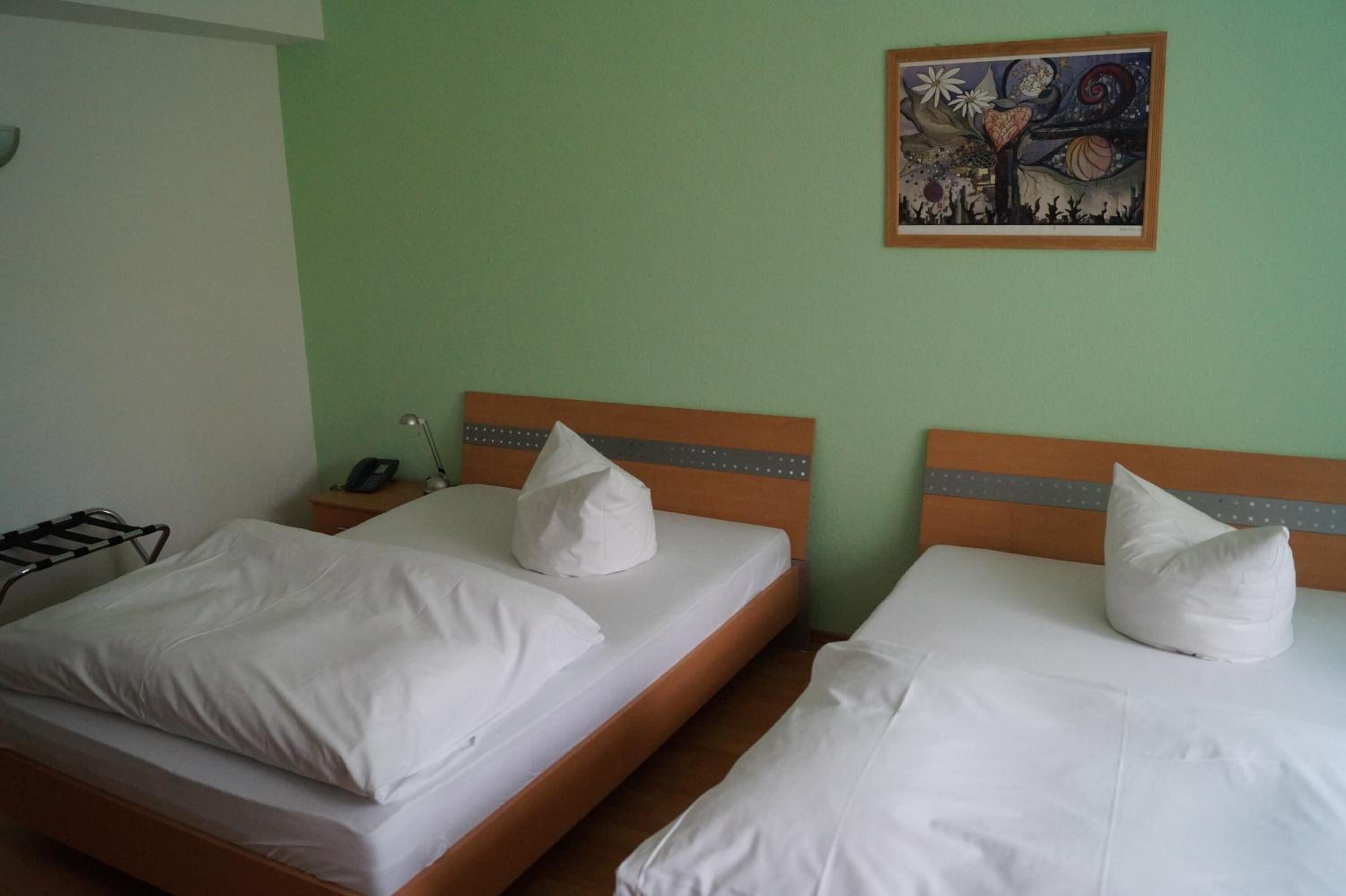 Hotelkamer met twee bedden, elk voorzien van witte lakens en kussens, een houten hoofdeinde en een nachtkastje met een telefoon.
