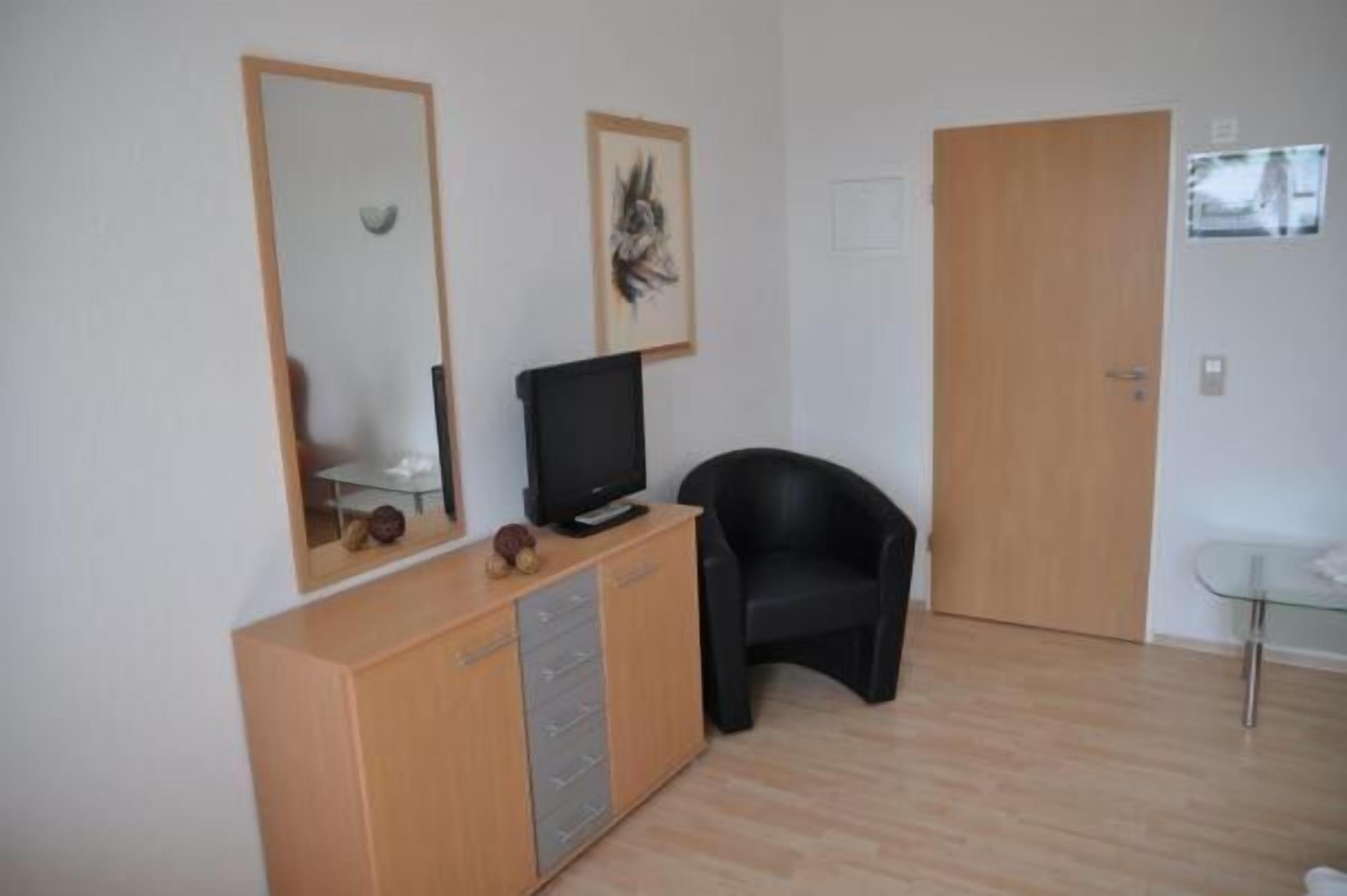 A room with a wooden cabinet, a black chair, a television on a stand, and a door.
