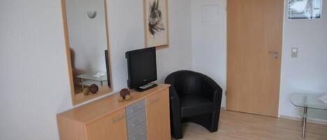 A room with a wooden cabinet, a black chair, a television on a stand, and a door.