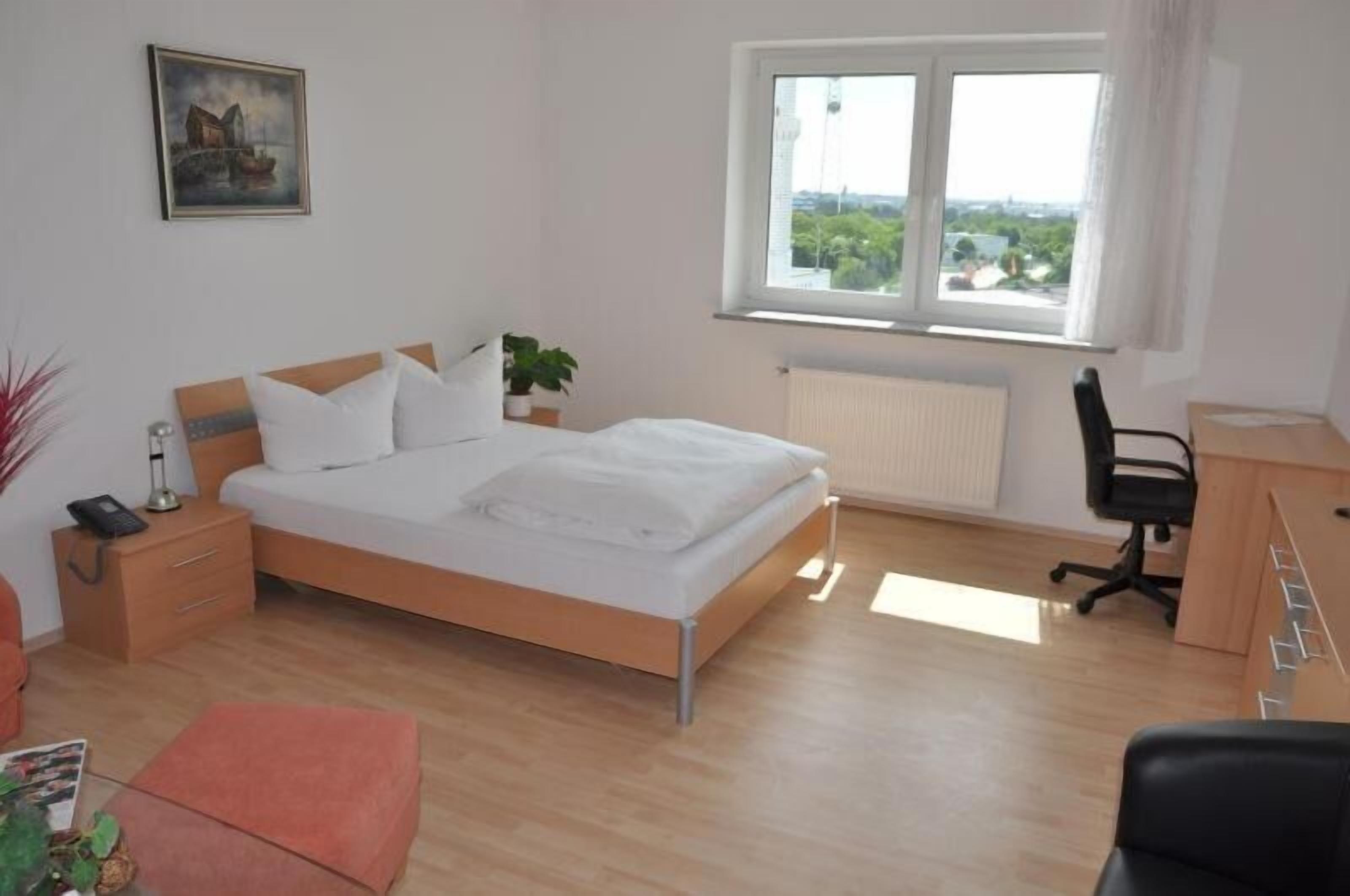 Un dormitorio con una cama, un escritorio, una silla, un ventanal y un radiador.