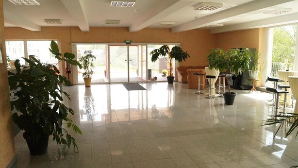 Un hall d’entrée spacieux, doté d’un sol carrelé, de plantes en pot et d’un espace détente avec des chaises et des tables.