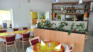 Un restaurant avec des tables et des chaises en bois, un coin bar avec des étagères remplies de bouteilles et des plantes en pot.
