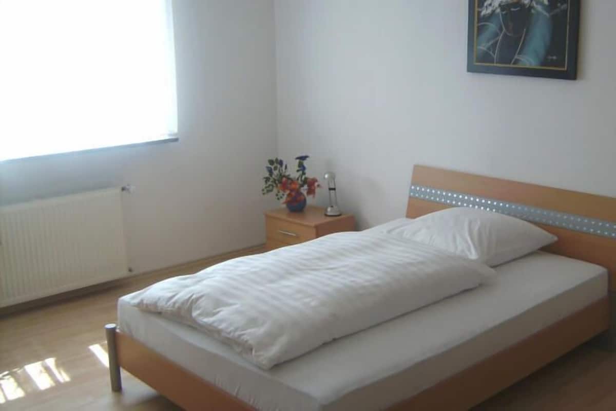 Ein Einzelbett mit weißer Bettwäsche, ein Holz-Kopfschild, ein Nachttisch mit Blumenvase und ein Wandbild.