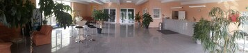 Un vestíbulo amplio con mostrador de recepción, zona de estar y plantas en macetas.