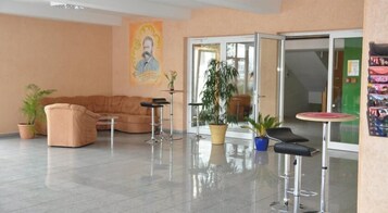 Un vestíbulo con un sofá, dos taburetes de bar, una planta en maceta y un cartel en la pared.