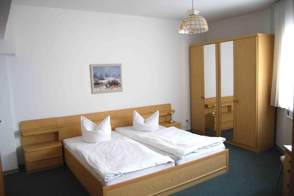 Ein Schlafzimmer mit einem hölzernen Bett, einem Nachttisch, einem Kleiderschrank und einer Pendelleuchte.