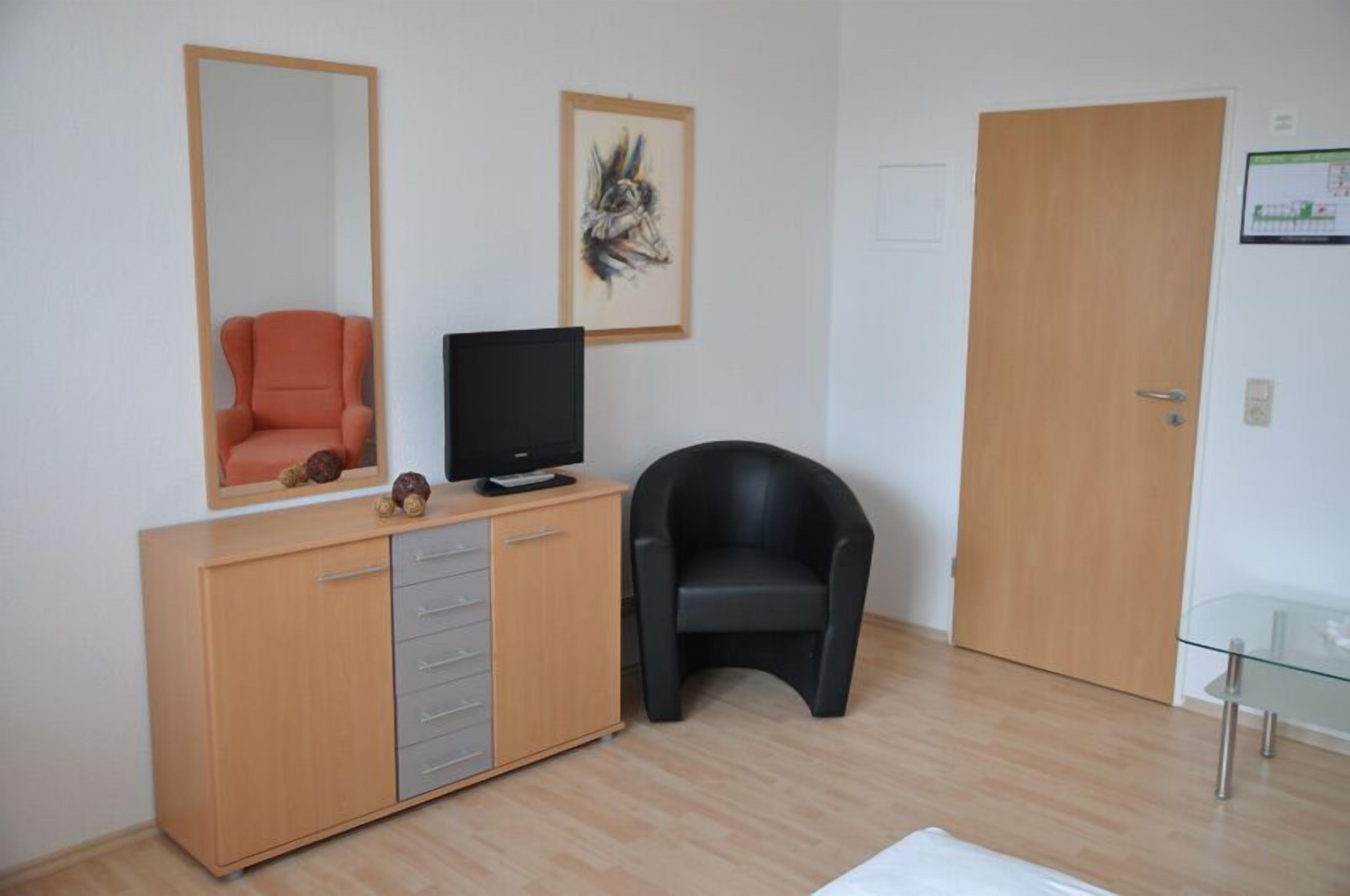 A room with a wooden cabinet, a black chair, a television, and a door.