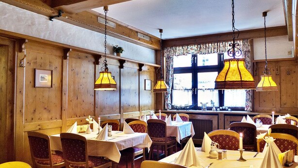 Un restaurante con paredes de madera, lámparas amarillas colgantes y mesas dispuestas con manteles blancos y sillas tapizadas en rojo.