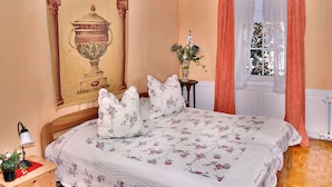 Un dormitorio con una cama grande, una mesita de noche, una lámpara, un jarrón con flores y una ventana con cortinas.