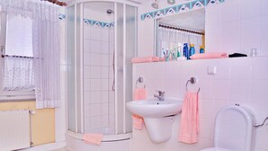 Baño con ducha, lavamanos e inodoro, con azulejos blancos y un espejo con artículos de aseo.