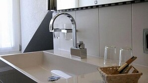 A modern kitchen with a large sink, a built-in stove, and a small countertop area with a basket of utensils. - HIP Hotel (Heidelberg)