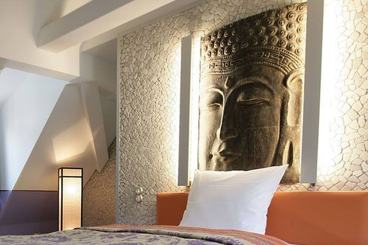 A bedroom with a large Buddha statue on the wall, a bed with a patterned bedspread, and a modern design with a sloped ceiling.