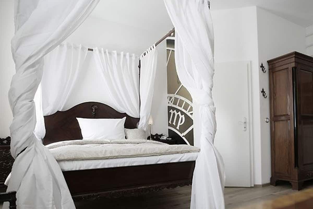 A four-poster canopy bed with a dark headboard, white bedding, and a small bedside table.
