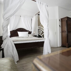 Una cama con dosel sobre cuatro soportes, con un cabecero oscuro, ropa de cama blanca y una mesita de noche pequeña.
