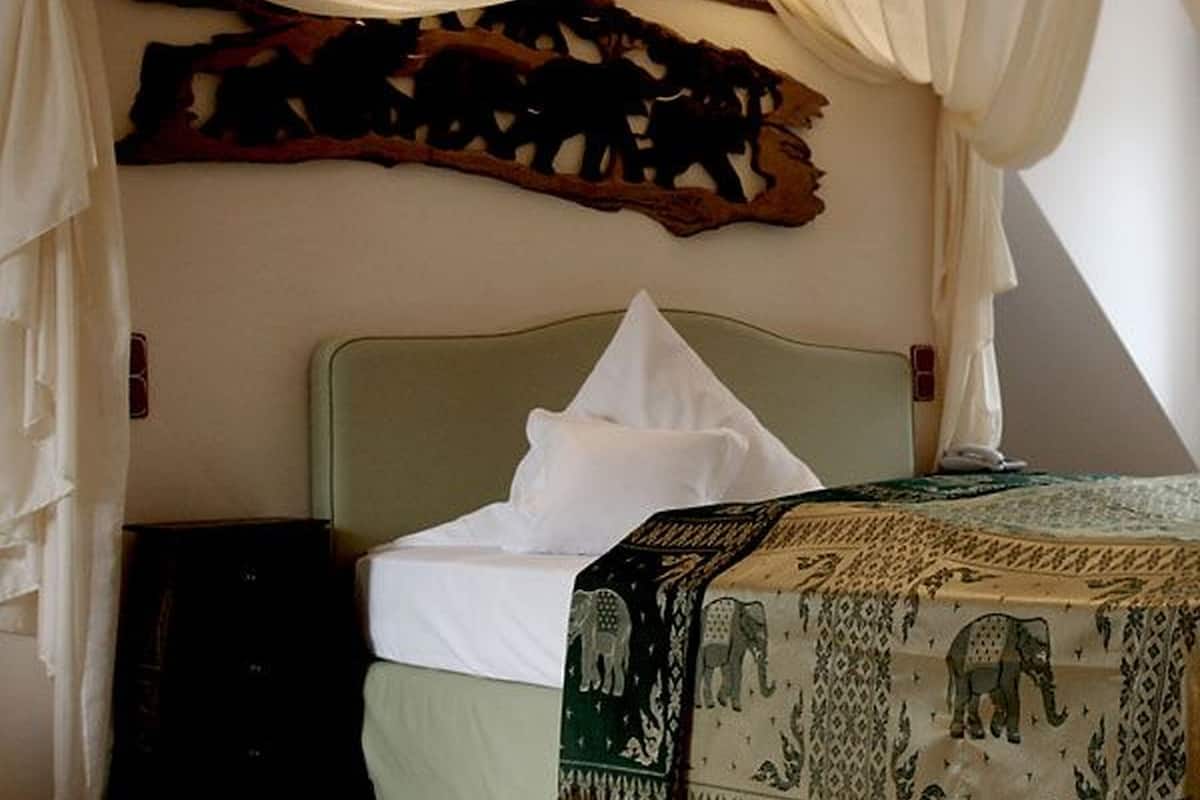 A bed with a green headboard, a white pillow, and a patterned blanket. There is a wooden wall art piece above the bed.