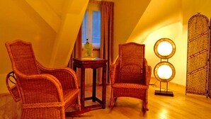 A cozy attic room with wooden flooring, two wicker rocking chairs, a small table, and a floor lamp. - HIP Hotel (Heidelberg)