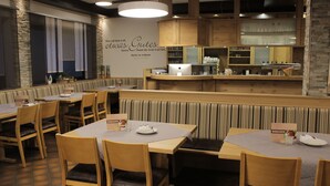 Un restaurant avec des banquettes et des tables en bois, un comptoir avec une caisse enregistreuse et un mur orné d’une citation allemande.