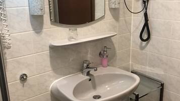 A bathroom with a white sink, a mirror, a hairdryer, and a glass shelf.