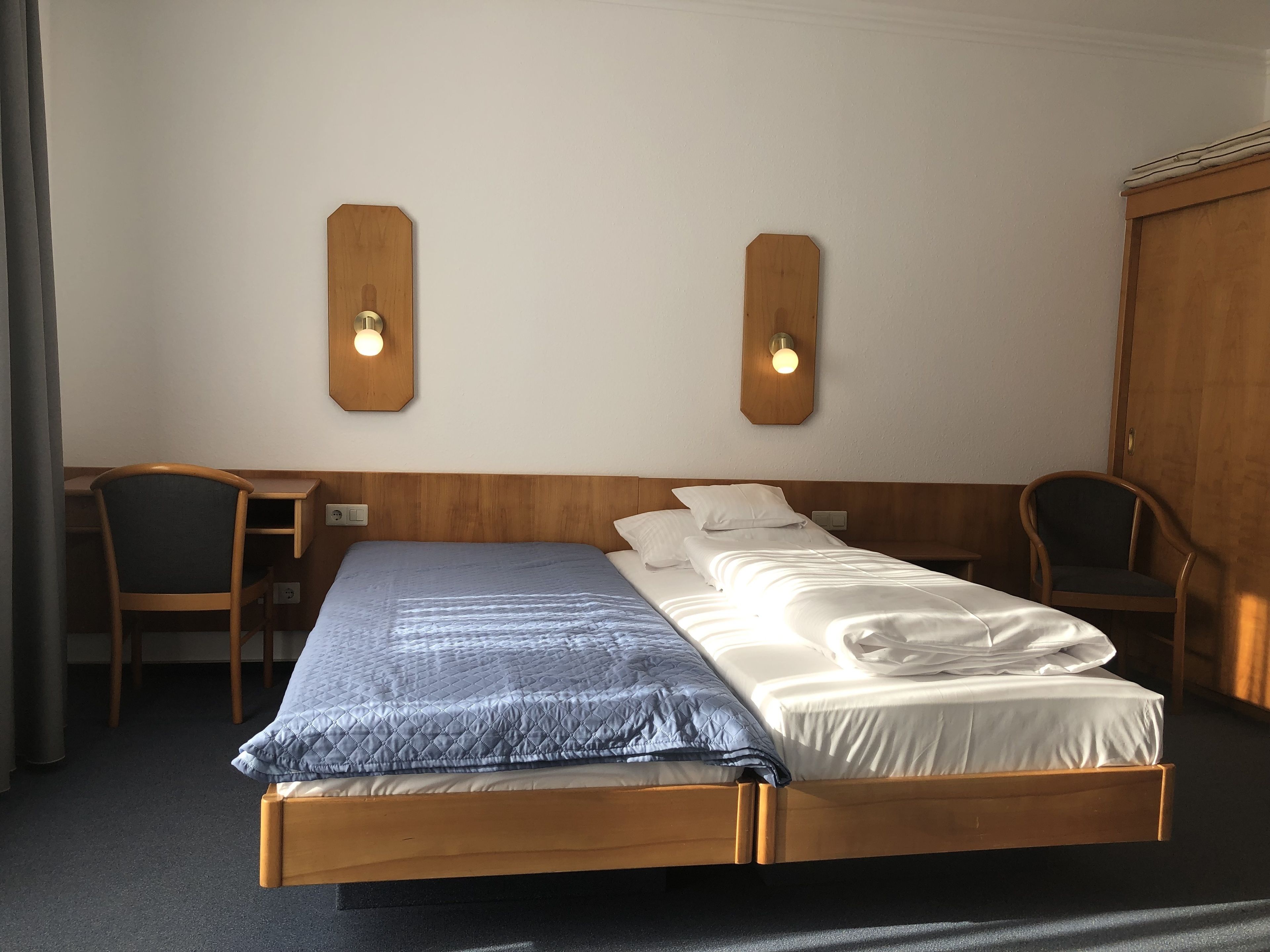 Un lit double avec une tête de lit en bois, deux tables de chevet et deux appliques murales.