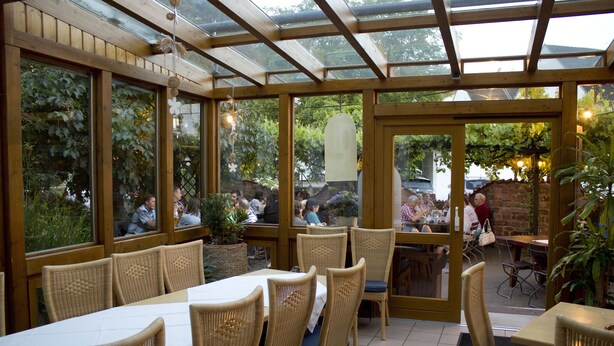Un espace extérieur abrité, aménagé pour les repas, avec des chaises et des tables en osier, de grandes fenêtres et une vue sur le jardin.