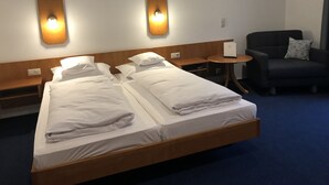 Une chambre d’hôtel avec deux lits simples, une petite table ronde, une chaise et des lampes fixées au mur.