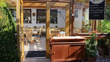 Un área de estar al aire libre con mobiliario de madera, una mesa de madera y un letrero que indica un menú con precios.