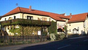 Un bâtiment avec un toit recouvert de tuiles rouges, une enseigne indiquant « Biergarten » et une clôture ornée de verdure.