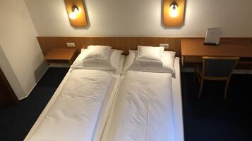 A double bed with two bedside tables, a desk with a chair, and wall-mounted lights.
