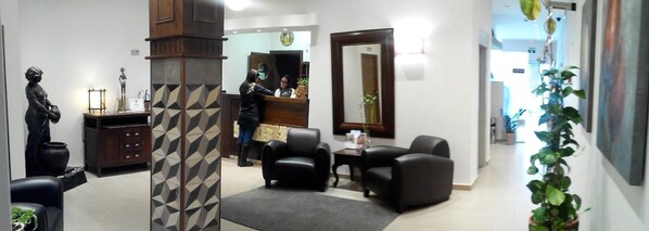 A reception area with a receptionist, black leather chairs, a wooden cabinet, and a large mirror.