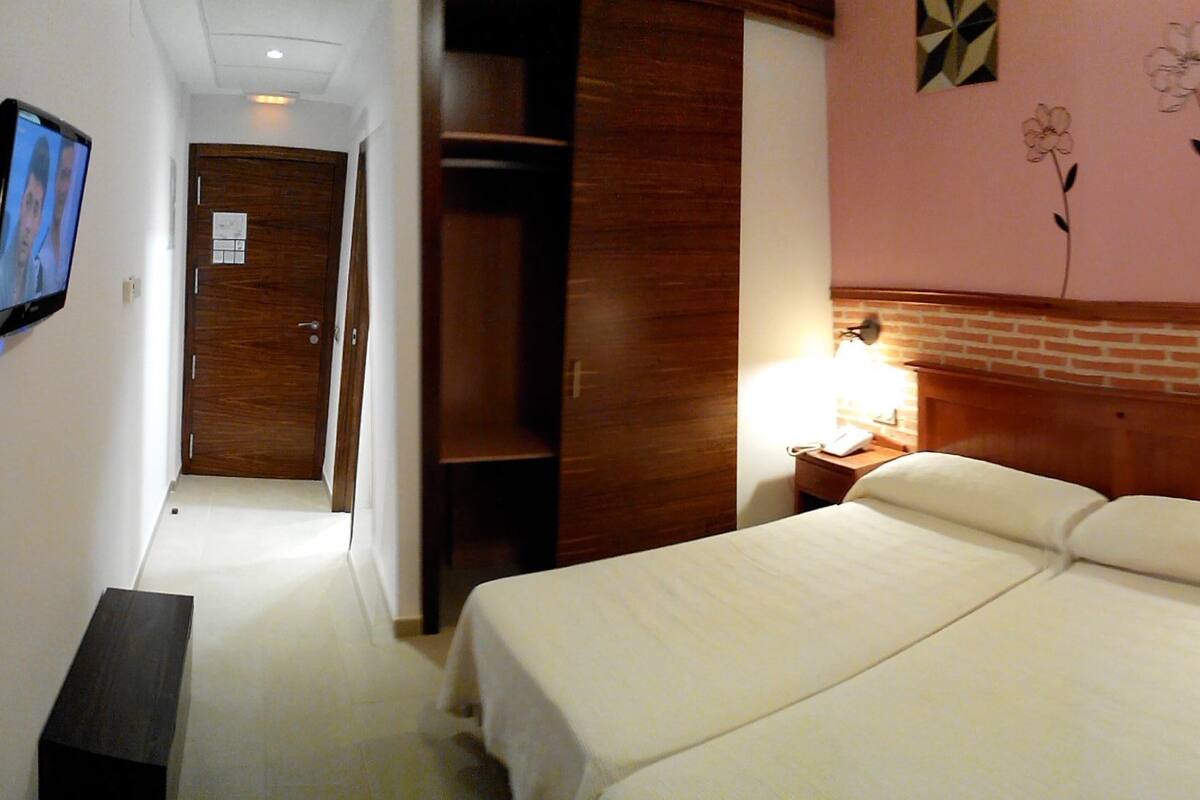 Una habitación de hotel con cama, mesita de noche, lámpara, televisor y armario de madera.