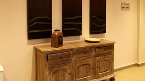 Een houten kast met lades en een vaas, met aan weerszijden drie verticale kunstwerken aan de muur.