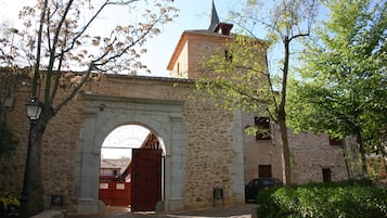 An arched stone gateway leading to a building with a tower and a red door.