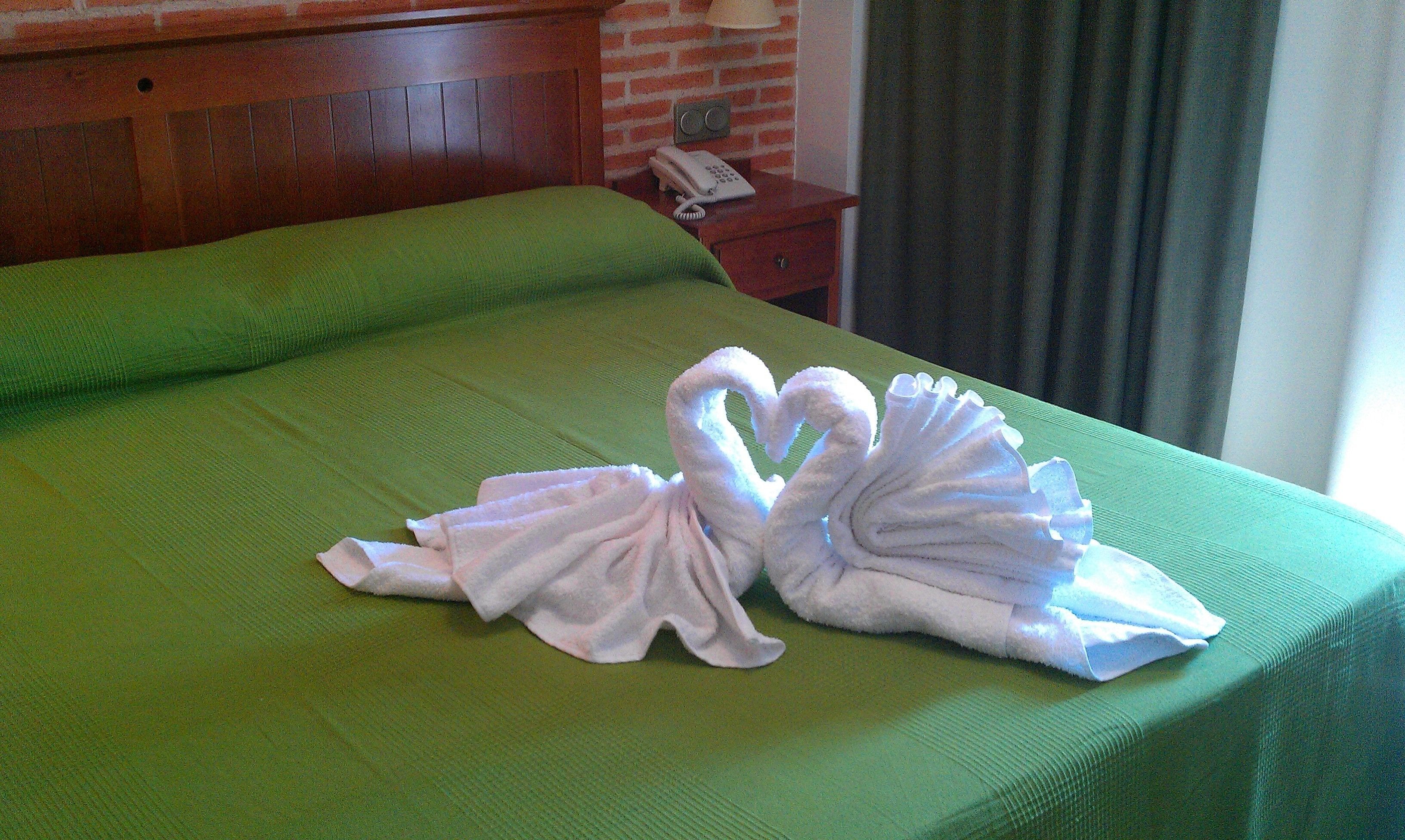 Una cama bien hecha con una colcha verde y dos toallas con forma de cisne.