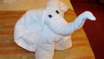 A plush elephant-shaped item on a bed with striped bedding.