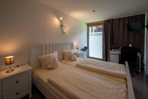 Habitación de hotel con dos camas, un escritorio, una silla, un televisor y una ventana con cortinas.