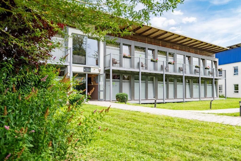 A modern building with multiple balconies, large windows, and a well-maintained lawn.