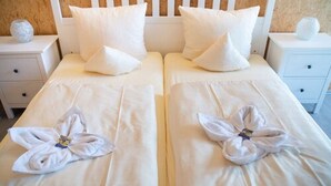 A double bed with white linens and pillows, a bedside table with a vase, and a towel arranged in a flower shape. - Hotel Vicinity (Hoppstaedten-Weiersbach)