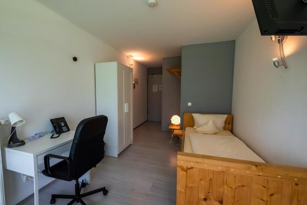 A compact room with a bed, a desk with a chair, a telephone, and a lamp.