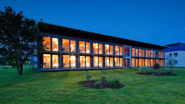 A modern building with large windows and a flat roof, surrounded by a well-maintained lawn. - Hotel Vicinity (Hoppstaedten-Weiersbach)