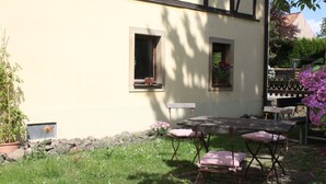 A patio with a table and chairs, a small window with a flower box, and a garden with various plants and flowers. - Landhotel Lindenschänke (Dresden)