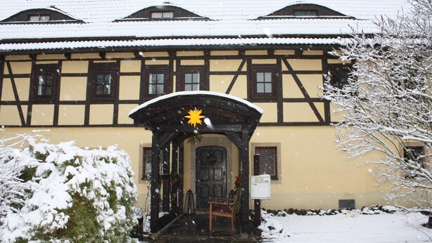 A traditional half-timbered building with a snow-covered entrance and a star decoration above the door. - Landhotel Lindenschänke (Dresden)