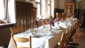 A long dining table set for a meal with chairs, a wooden cabinet, and a window with curtains. - Landhotel Lindenschänke (Dresden)
