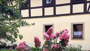 A traditional half-timbered building with a garden featuring pink flowers. - Landhotel Lindenschänke (Dresden)