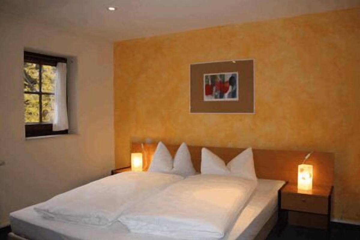 A hotel room with a large bed, two bedside tables, a window, and a framed picture on the wall.