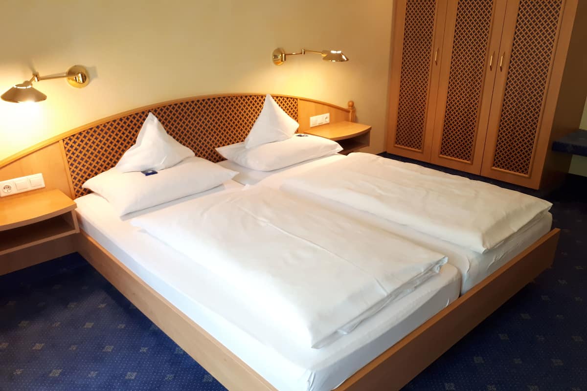 Una cama doble bien hecha con ropa de cama blanca, un cabecero de madera con diseño estampado, lámparas de noche y un armario con diseño de celosía.